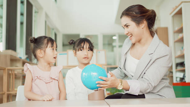 istock Elementary and preschool girls learning world map with model globe with teacher in Montessori education school 1613287925