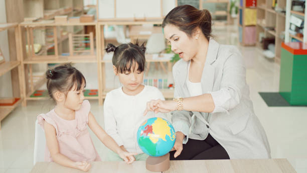 istock Elementary and preschool girls learning world map with model globe with teacher in Montessori education school 1613288977