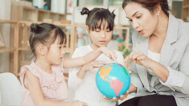 istock Elementary and preschool girls learning world map with model globe with teacher in Montessori education school 1613292780