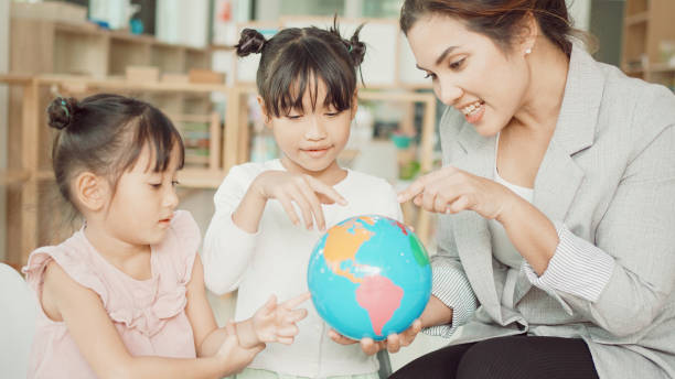 istock Elementary and preschool girls learning world map with model globe with teacher in Montessori education school 1613293309