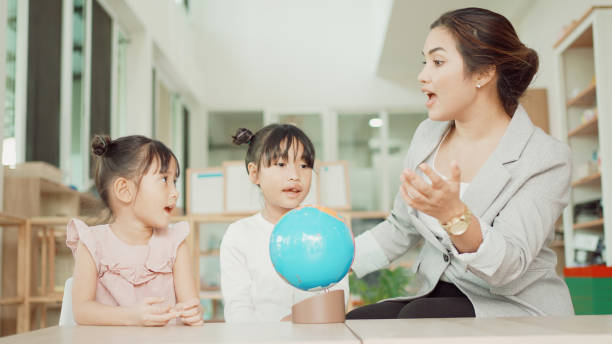 istock Elementary and preschool girls learning world map with model globe with teacher in Montessori education school 1613293321