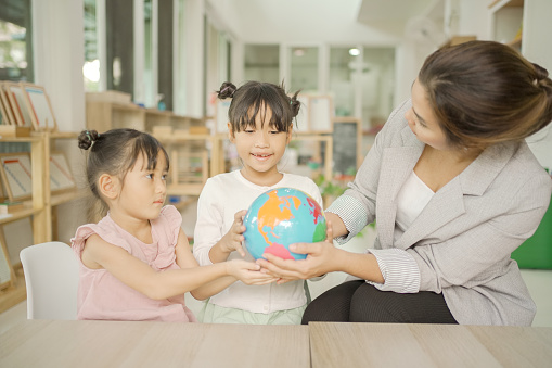 Elementary and preschool girls learning world map with model globe with teacher in Montessori education school