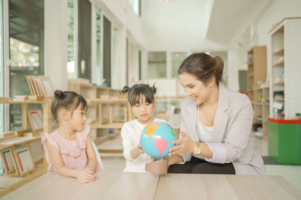 istock Elementary and preschool girls learning world map with model globe with teacher in Montessori education school 1613298078