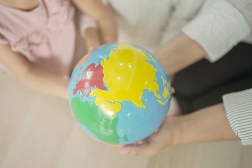 Elementary and preschool girls learning world map with model globe with teacher in Montessori education school