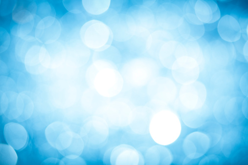 Blurred, illuminated blue holiday sparkles abstract, patterned background with darker corners and a bright center.  The image is vibrantly colored with a textured effect and defocused light.