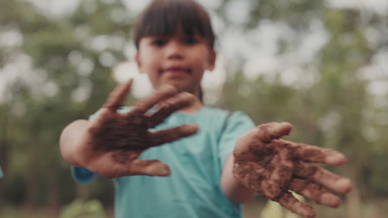 Portrait of young girl showing dirty hands while standing in forest scene.