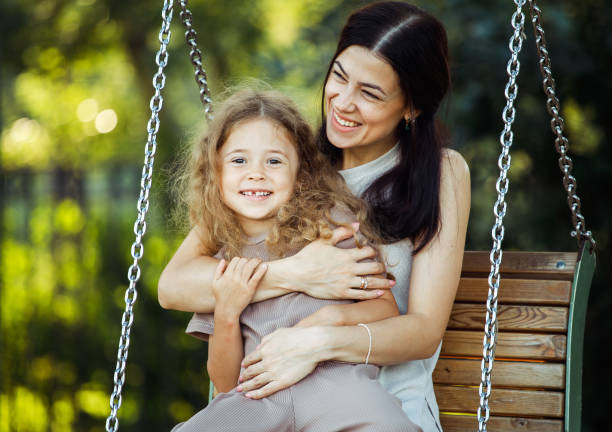 mama und tochter schaukeln auf einer schaukel. kaukasische frau und kleines mädchen haben spaß auf dem spielplatz. - netting women brown hair outdoors stock-fotos und bilder