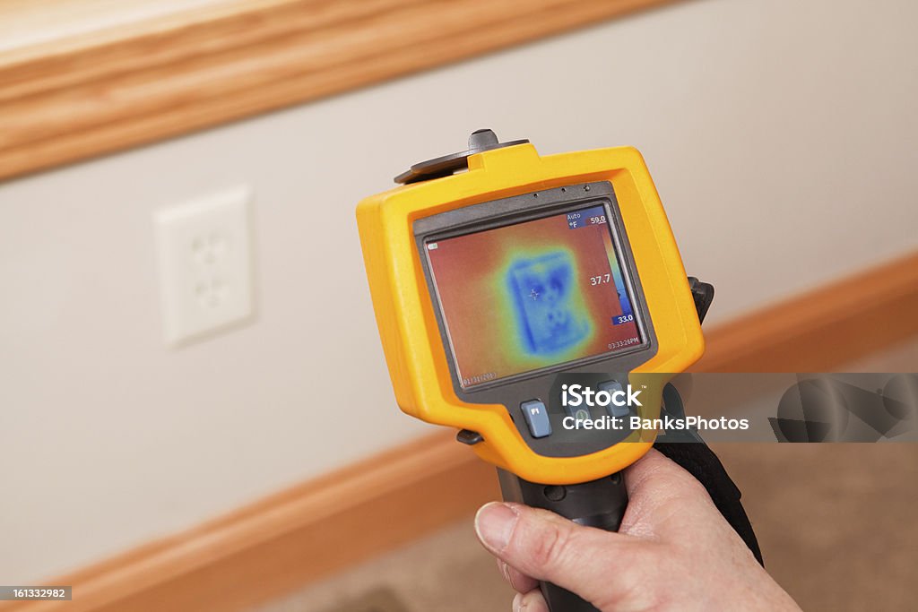 Infrared Thermal Imaging Camera Pointing to Wall Outlet An infrared thermal imaging system being used during a home energy audit. The camera is pointed to a wall outlet, on an exterior wall, showing the blue (cold) area within the home’s insulation. The center target area reads 37.7 degrees with a range of 33 to 59 degrees in the area.  Energy audits are performed to determine how efficient the house is and to suggest steps to increase energy efficiency. Thermal Image Stock Photo