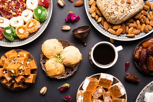 Middle Eastern Sweets, Turkish Delights and Black Coffee on black background. Arab dessert assortment, rahat lokum, halva, sherber, pismaniye with nuts and dates and cup of coffee.