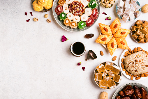 Middle Eastern Sweets, Turkish Delights and Coffee on white background, copy space. Arab dessert assortment, rahat lokum, halva, sherber, pismaniye with nuts and dates and cup of coffee.