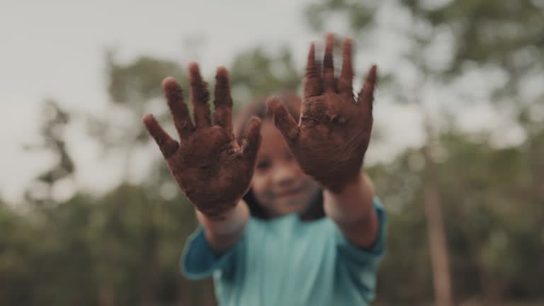 Portrait of young girl showing dirty hands while standing in forest scene.