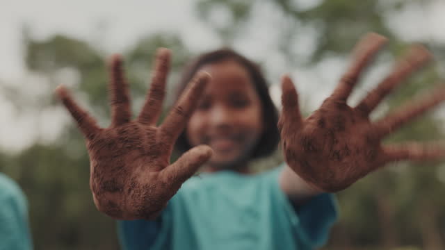 Portrait of young girl showing dirty hands while standing in forest scene.