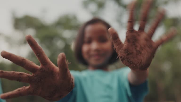 Portrait of young girl showing dirty hands while standing in forest scene.