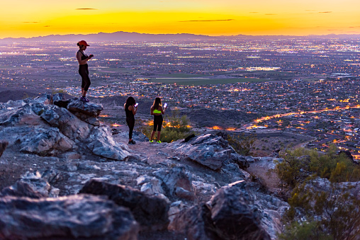 As the daylight fades, sightseers at Dobbins Lookout on South Mountain, a popular tourist destination, snap pictures of the lights of Phoenix coming awake.