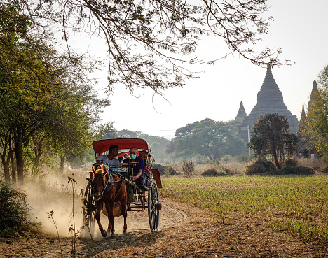 Bagan, Myanmar - Feb 18, 2016. Horse cart carrying tourists on dusty road in Bagan, Myanmar. Bagan is an ancient city and one of Asias most important archeological sites.