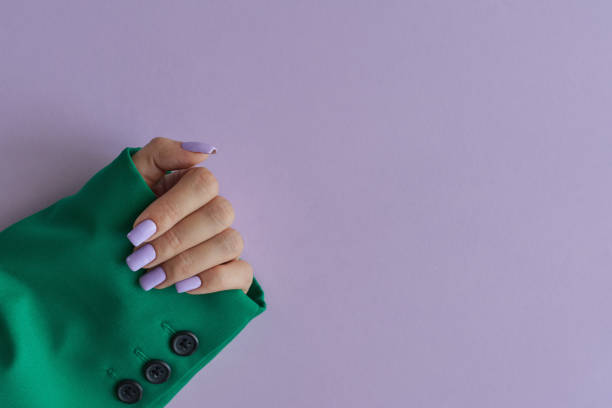 紫の背景に緑のジャケットを着た紫色の爪を持つ女性の手。ゲリッシュマニキュア