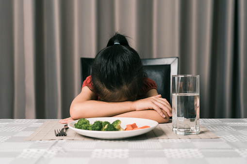 Little cute kid girl refusing to eat healthy vegetables. Children do not like to eat vegetables.