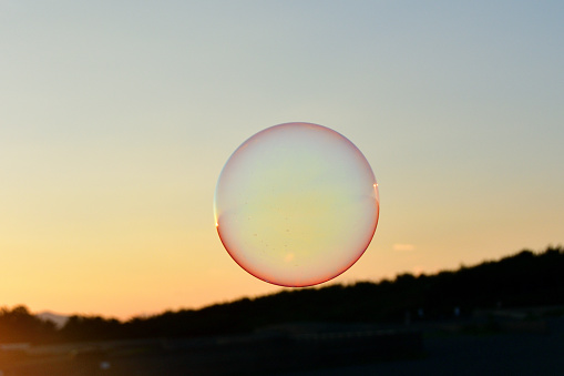 A perfect round soap bubble flying in the sunset sky.
