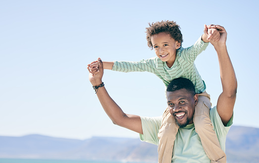 Black family, man and a son sitting on shoulders while outdoor in nature together during a beach vacation. Love, sky or kids with a father or parent carrying his child while walking on the coast