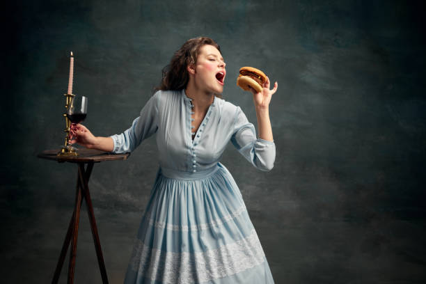 princesa. retrato da mulher aristocrática usando vestido histórico azul comendo hambúrguer grande. arte gastronômica contemporânea. - mirror women baroque style fashion - fotografias e filmes do acervo