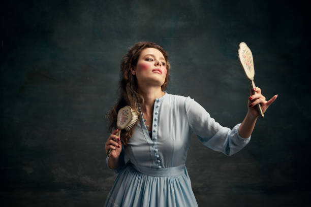 beauty. portrait of charming aristocratic woman wearing blue historical dress holding vintage mirror in hand and brushing her hair. - mirror women baroque style fashion imagens e fotografias de stock