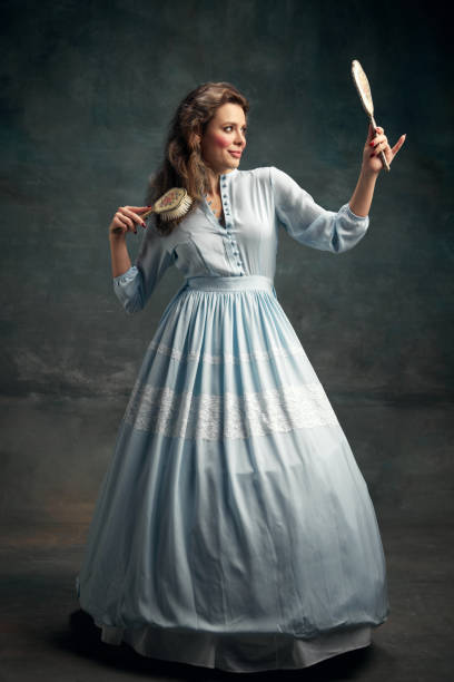 full-lenght portrait of charming aristocratic woman wearing blue historical dress holding vintage mirror in hand and brushing hair. - mirror women baroque style fashion imagens e fotografias de stock