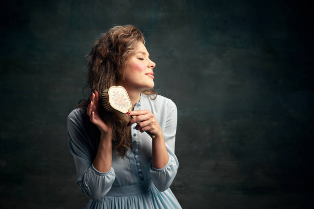 portrait charming aristocratic woman wearing blue historical dress holding vintage hairbrush in hand and brushing her hair. - mirror women baroque style fashion imagens e fotografias de stock