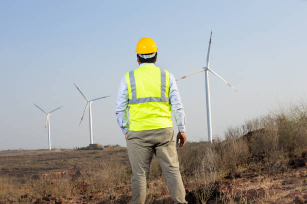 istock India engineer using laptop to control and maintain windmill farm operation to generate electricity, Asian man wearing yellow helmet and vest working at wind turbine farm, Clean and green energy. 1613590308