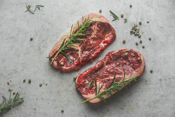istock Raw marble black angus steak with rosemary and green pepper on grey concrete kitchen table. 1613591937