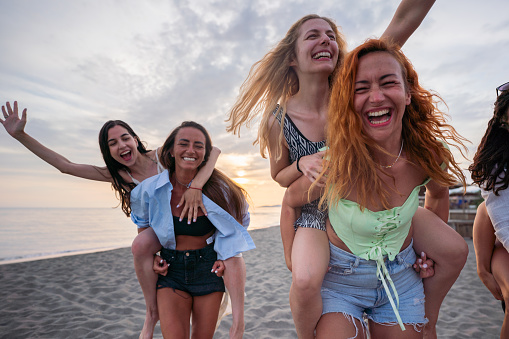 Group of happy female friends having fun while piggybacking on the beach