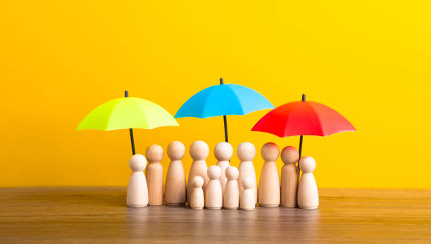 istock Many wooden people figures under umbrella on yellow background. 1613642707