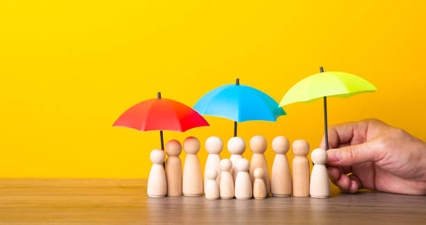 istock Many wooden people figures under umbrella on yellow background. 1613642712