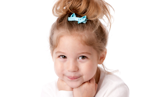 A head and shoulders image of a confident smiling real caucasian little girl. She has brown hair and brown eyes.