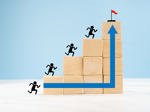 Common goal success concept. Business achieving goal, objective target, and team. Teamwork rises to target and achieves a successful business. Red flag icon on wooden cubes with a blue background