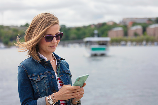 A woman outdoors at the quay in Stockholm, buying a ticket for an automated ferry using the mobile phone.