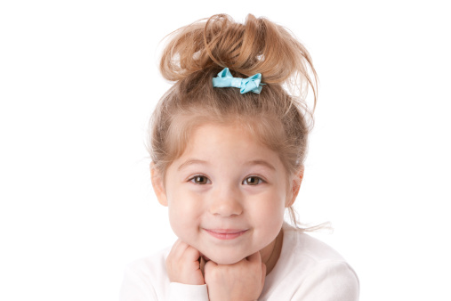 A head and shoulders image of an adorable smiling caucasian little real girl with her hair up and a blue bow.