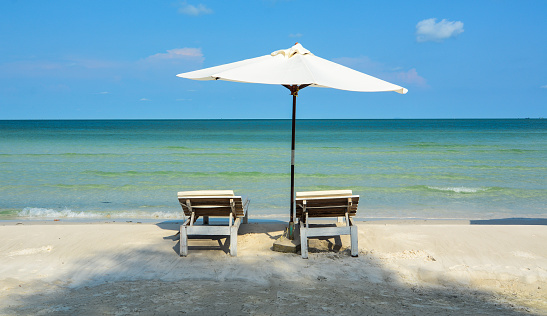 Three plastic Adirondack chairs on the edge of a Cape Cod beach.