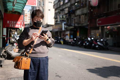 Asian Chinese female tourist searching location with mobile app at downtown district of Taipei, Taiwan