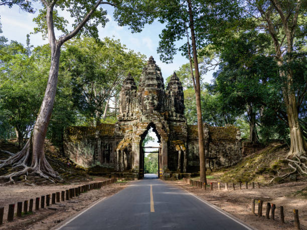Asphalt road through the North Gate of Angkor Thom. Ancient Civilisation Stone Entrance Gate with Religious Khmer Face Sculpture on Top of the North Entrance Gate towards the famous Angkor Thom Temple Area. Hasselblad X2D 102 MPixel High Detail Travel Shot with enough room to crop. Angkor Thom, Angkor Wat Area, Cambodia, South East Asia.