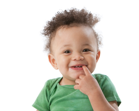 A head and shoulders image of a laughing Black or African American toddler boy in a green shirt. He has his finger in his mouth.