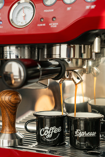 Barista coffee pouring from professional espresso machine with wooden tamper in cafe close-up