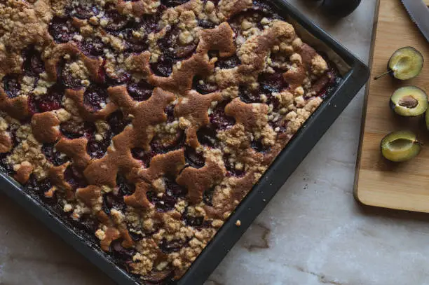 Traditional german plum crumble cake or streusel kuchen with plums. Served fresh and warm on a baking sheet on kitchen counter from above.