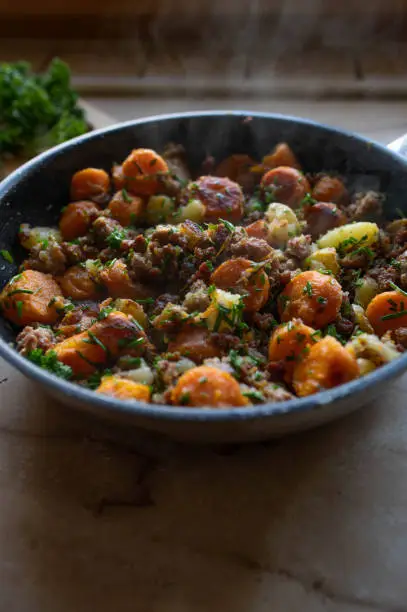 Homemade country food with pan fried potatoes with carrots, onions, chives and ground pork in a hot and steaming frying pan.