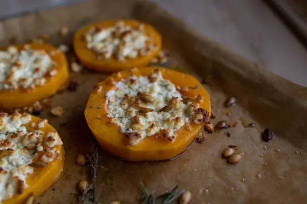 Healthy gluten free and zero waste food with a oven roasted butternut squash filled with feta cheese and herbs and topped with pumpkin seeds. Served ready to eat on baking sheet. Closeup