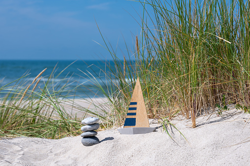 Model of a sailboat and a pile of stones in the sand dunes. Symbol for a boat journey.