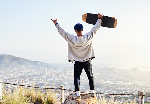 Skateboard, freedom and mountains with man cheering for fitness, sports and adventure. Happiness, commitment and training with gen z guy skating in outdoors for travel, wellness and summer break