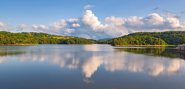 white clouds reflecting in the blue water of Crescent lake and forest-covered hill in the Morvan in France