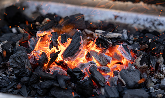 Ember of charcoal on a barbeque grill. Close-up of fire, glowing charcoal and hot embers. Summer, heat, temperature, leisure activity, outdoors, barbecue season.