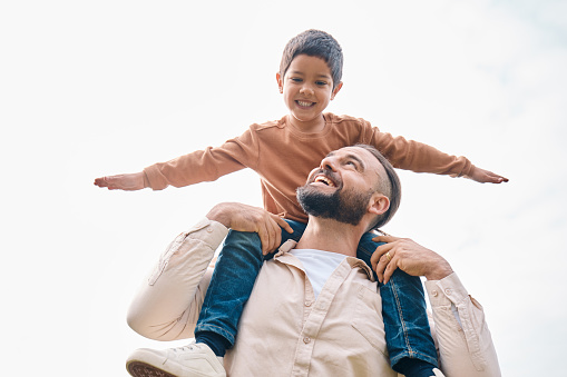 Family, kids and boy sitting on the shoulders of his father outdoor while bonding from below. Fun, children and love with a man carrying his son outside while spending time together being playful