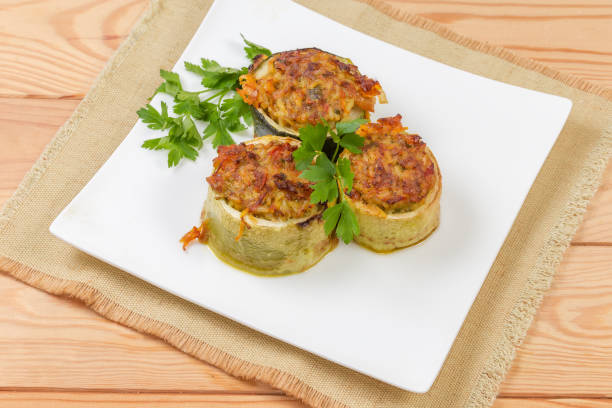 Cooked pieces of zucchini stuffed with filling of the boiled rice with minced meat on the square dish on a place mat on a rustic table